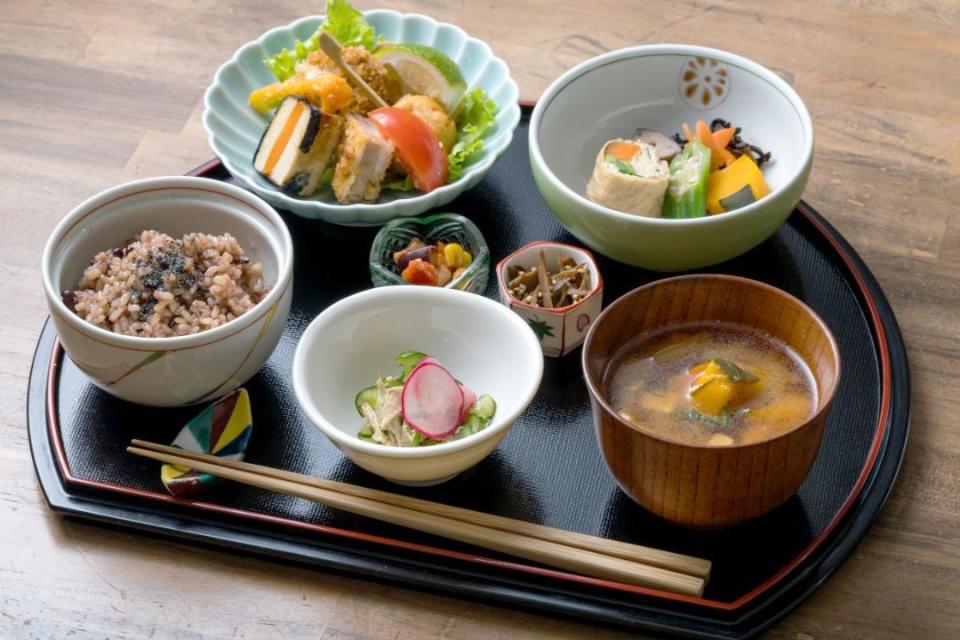 写真：手前左から雑穀米ごはん、小鉢、かぼちゃの味噌汁・奥の左から野菜と豆腐のフライ、オクラやかぼちゃの煮物があるセット料理