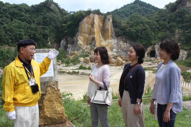 写真：黄色い上着のガイドが3人の女性に山の景観を説明している
