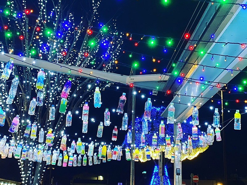 写真：駅前の通路屋根に色とりどりのペットボトルランタンや電球が装飾されている夜景