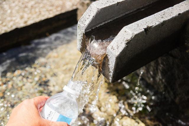 写真：透明な水が流れ出ているセメント造りの取水口に、ペットボトルを当てている手元