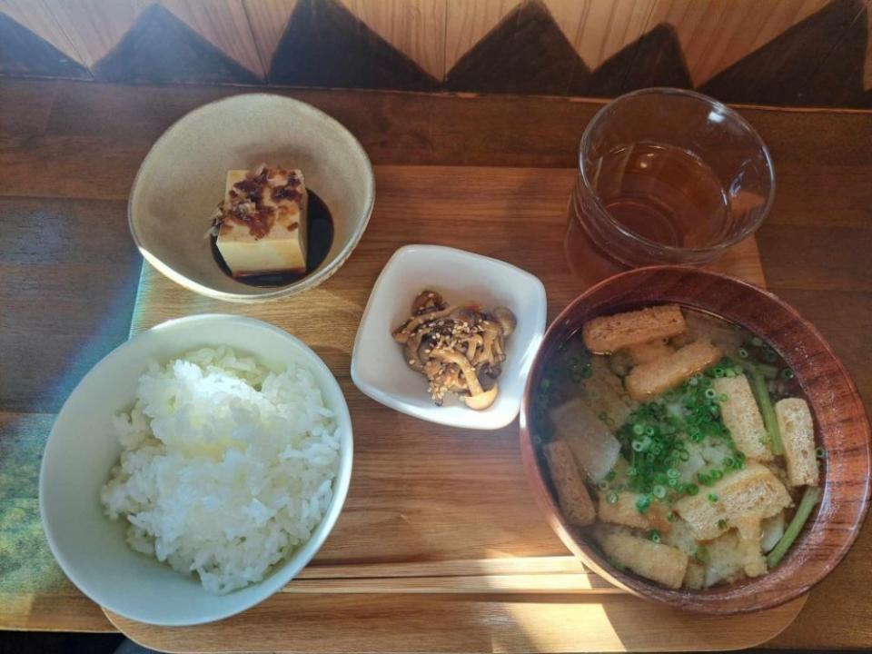 写真：ご飯、油揚げと青菜のお味噌汁、キノコの炒め物、ひややっこ、お茶がトレイにセットされている様子