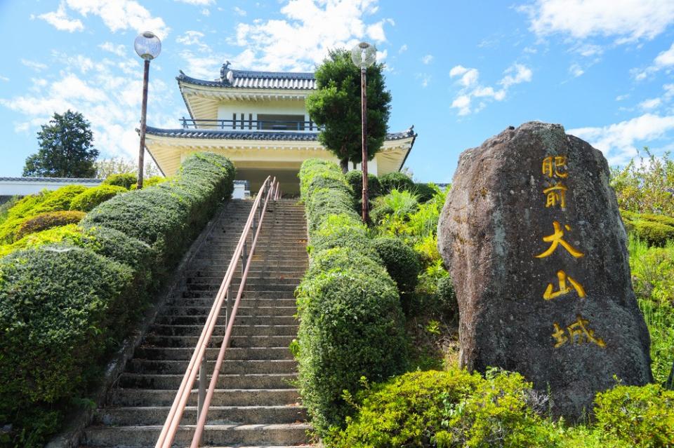 写真：肥前犬山城展望所を階段下から見上げた様子。階段の向かって右に「肥前犬山城」と刻まれた石碑が立っている