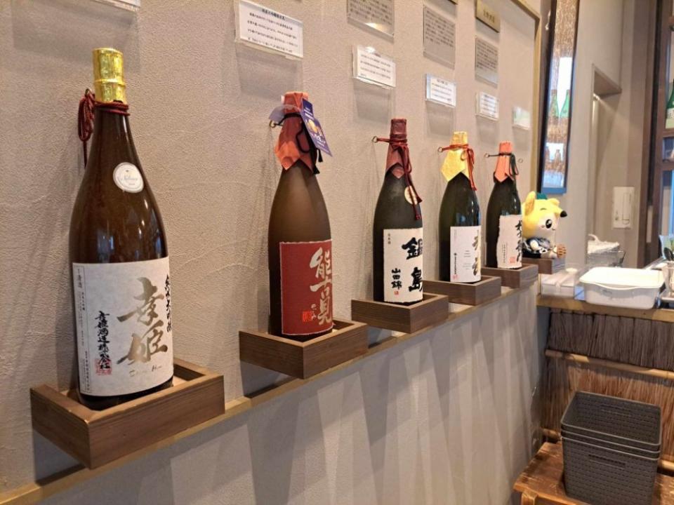 写真：壁面に5本並んでディスプレイされた日本酒の瓶。手前から幸姫、能古見、鍋島、光武、蔵心権右衛門