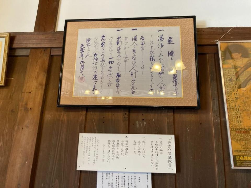 写真：「秀吉公温泉掟書」を収めた額が壁にかけられている様子。その下に解説パネルが掲示されている