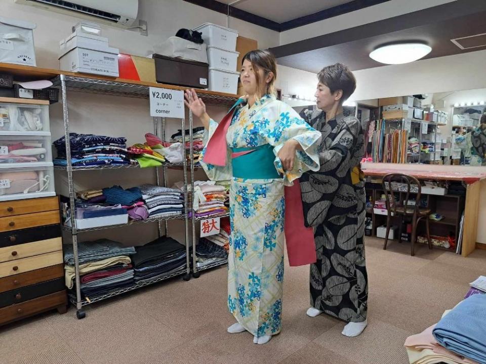 写真：楽屋で、浴衣を着付けしてもらっている女性ライター。指導役の女性が帯を結んでいる最中