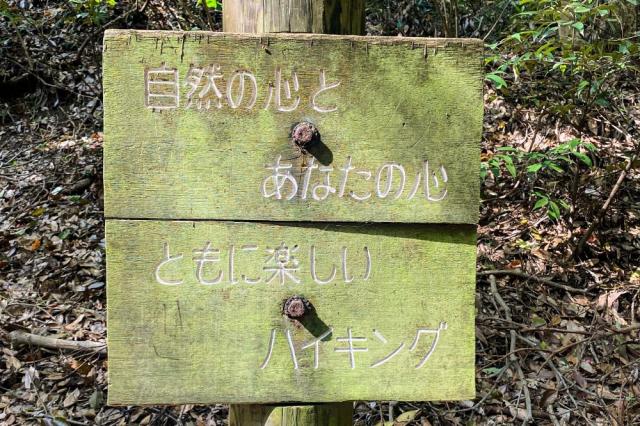 写真：木の柱に打ち付けられた「自然の心とあなたの心」「ともに楽しいハイキング」と書かれた看板