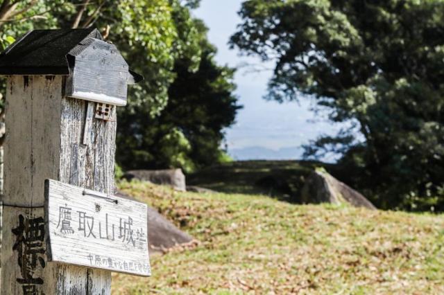 写真：「鷹取山城址」の標。背景に山頂から見おろす眺望が見える