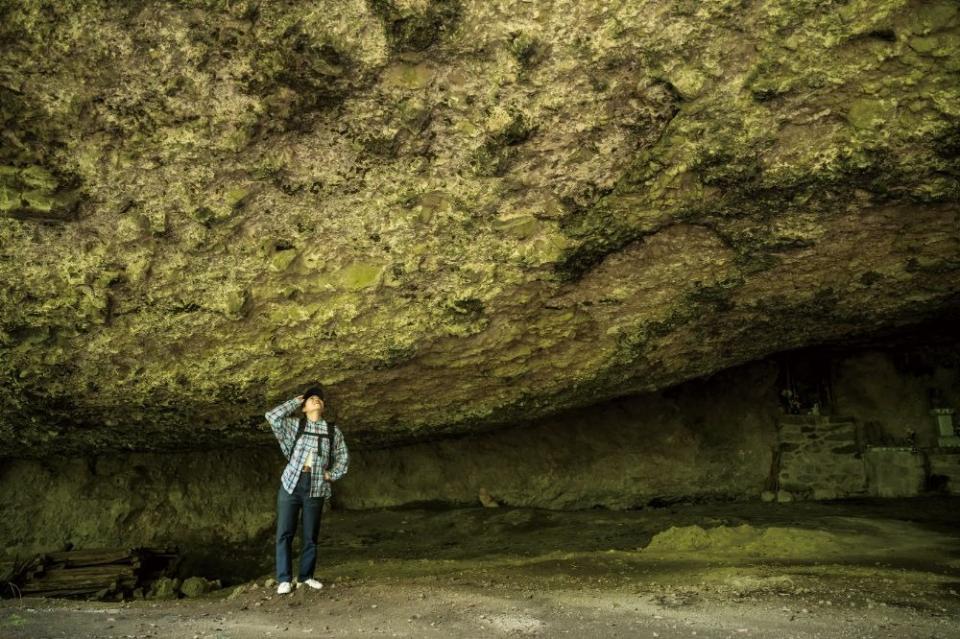 写真：洞窟の中で天井を見上げている女性。画面右側にお地蔵様が祀られている