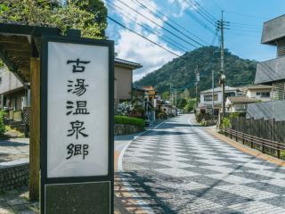 写真：古湯温泉郷の看板が道端に立っている風景。道路は石畳で、奥に山が見える