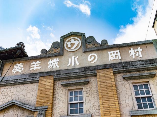 写真：村岡総本舗・羊羹資料館の看板。右から左へ横書きで「村岡の小城羊羹」と書いてある