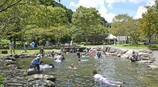 写真：川の水を張った夏の河川プールの風景。たくさんの家族連れが水遊びを楽しんでいる