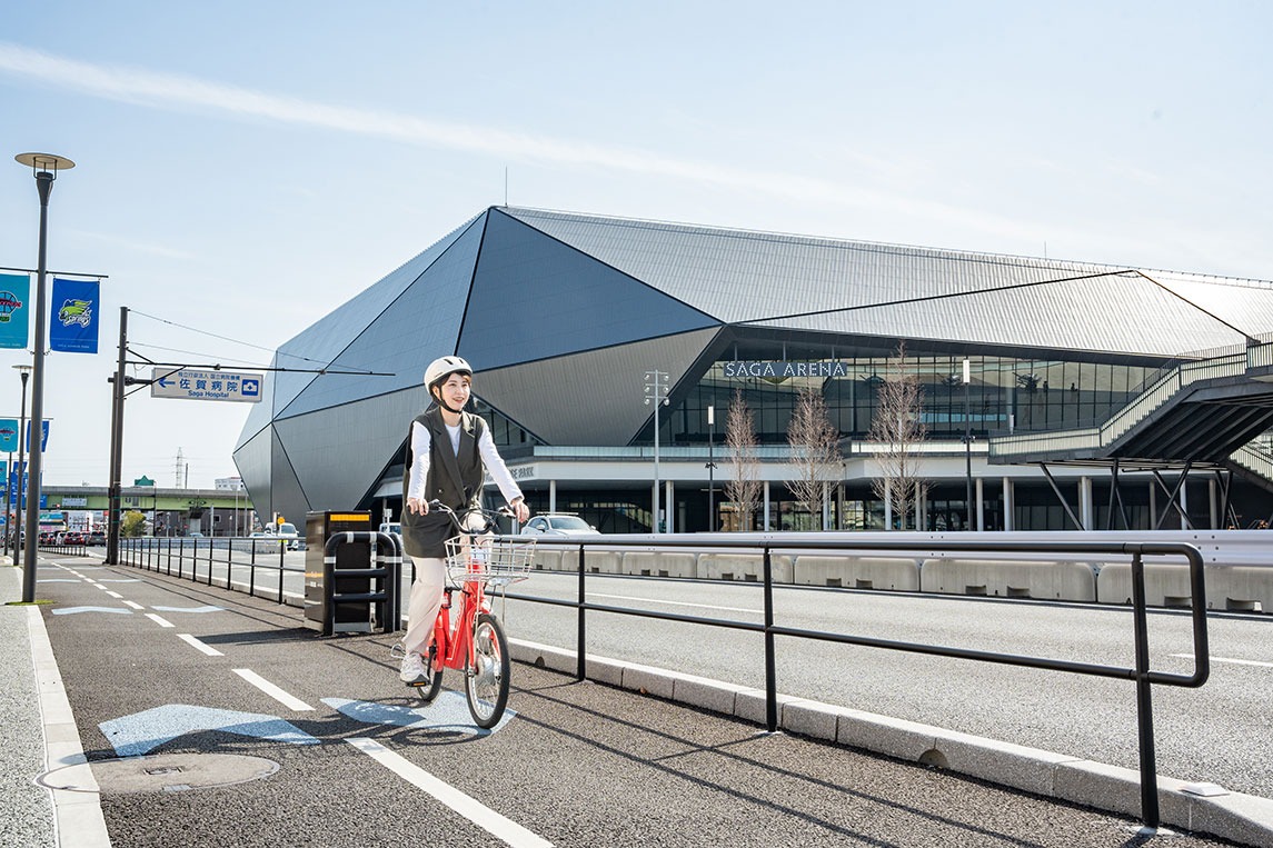 写真：佐賀アリーナ前の道路をチャリチャリの赤い自転車に乗った女性が走行している様子