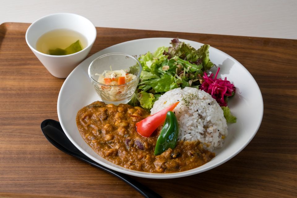 三角にカットされたピーマン、パプリカが乗り、サラダがそれられたカレー