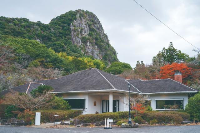 手前に茶色の屋根と白い壁の店舗があり、奥に山と紅葉が見えるが風景画像